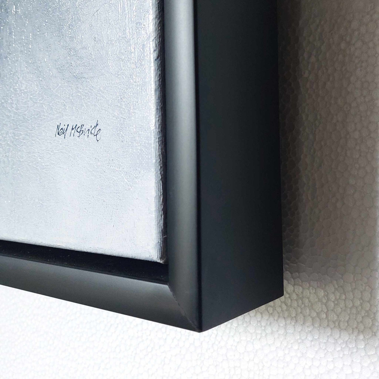 Close-up of a black framed artwork with a textured background signed Neil McBride
