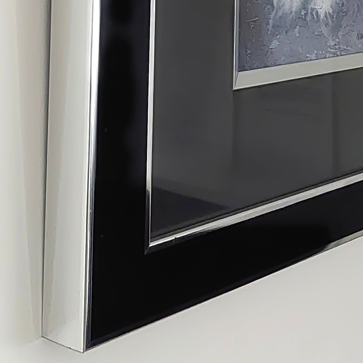Close-up of a glossy black framed picture, titled King Art, with a silver inner border and a silver outer frame, mounted on a white wall.